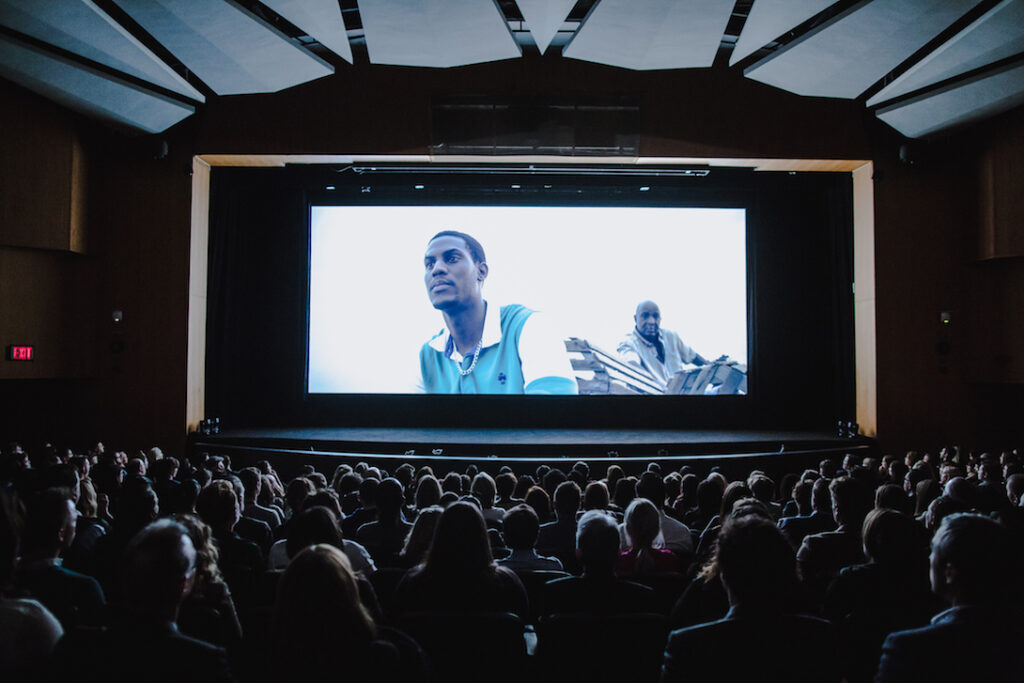 inside a movie theater with a projected image of a man on the screen