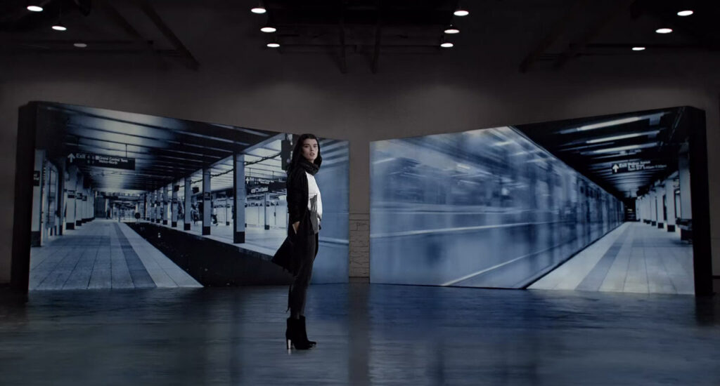 woman standing in a room with projected scenes on the walls behind her