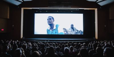 inside a movie theater with a projected image of a man on the screen